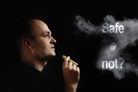 E-cigarette safe or not. A young man smokes an electronic cigarette against a Photos