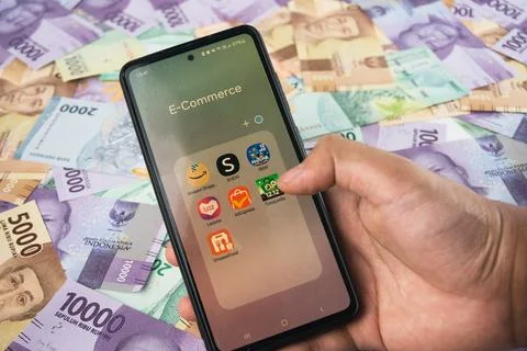E-Commerce Apps Displayed on Smartphone Amid Colorful Indonesian Banknotes Stock Photos