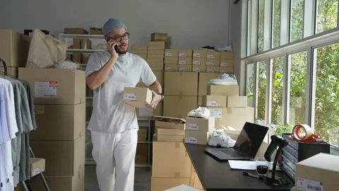 E-commerce business owner using phone and looking at laptop in store warehouse. Stock Footage 174077203