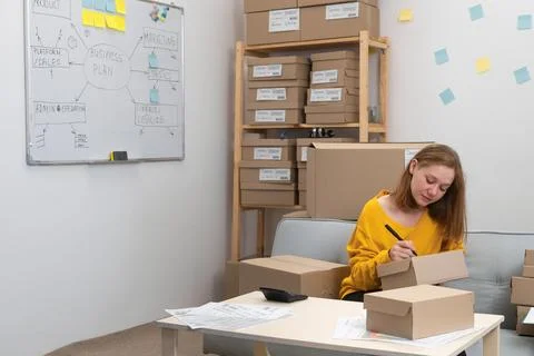E-commerce owner preparing parcels for shipment in home office, writing add.. Stock Photos