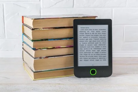 E-reader near stack of paper books on a wooden table. Copy space on display. Stock Photos