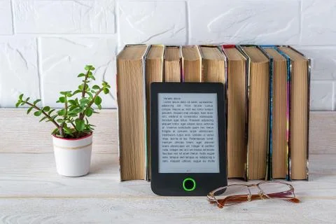 E-reader near stack of paper books, potted plant and vision glasses. Stock Photos