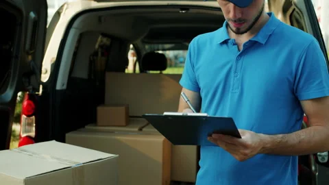 E-shop courier signing documents counting parcels in van working outside alone Stock Footage 157311637