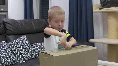 Eager Boy Opens Package with Scissors at Home Stock Footage 310655110