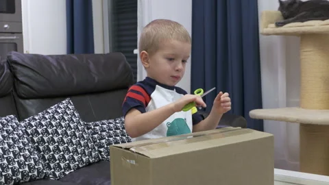 Eager Unboxing: Blond Boy Opens Cardboard Box at Home with Scissors Stock Footage 304295272