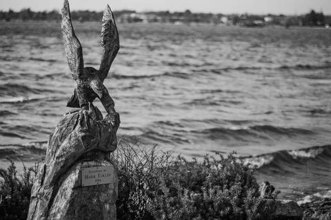 An Eagle Carved From A Large Tree Rests At The Edge Of A Lake, Black And White Stock Photos