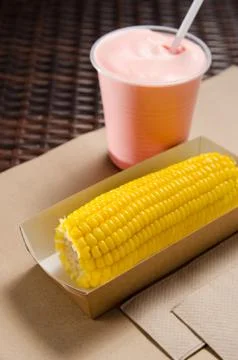 An ear of boiled corn in an eco-friendly cardboard box next to a milkshake Foto stock