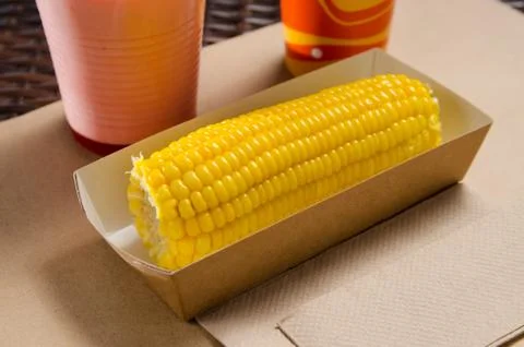 An ear of boiled corn in an eco-friendly cardboard box next to a milkshake an Foto stock