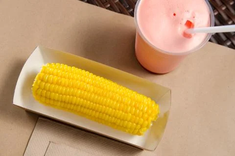 An ear of boiled corn in an eco-friendly cardboard box next to a milkshake Foto stock