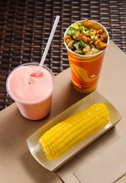 An ear of boiled corn in an eco-friendly cardboard box next to a milkshake an Stock Photos