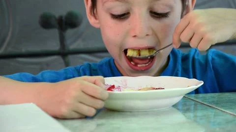 Early age boy sitting at the table and eat with a spoon from a deep dish Stock Footage 60578860