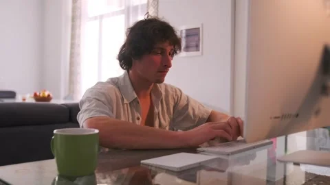 Early morning freelance work, Casual man working at sunlightlit desk, Relaxed Stock Footage 331281053