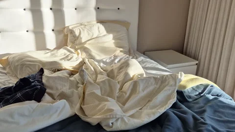 Early morning sunlight casting long shadows across an unmade bed Stock Footage 331020417