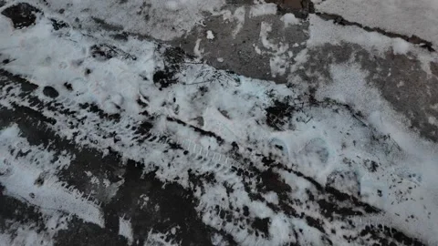 Early spring thaw on a frozen road. Footprints and tracks mark the slippery, mel Stock Footage 330936853