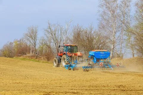 In early spring, the tractor sows the field with grain. Modern machinery works Stock Photos