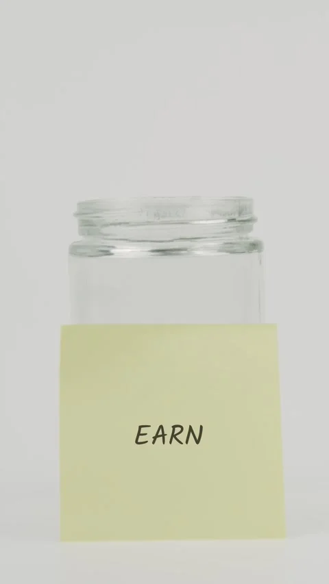 Earn text or word on yellow sticky note attached to glass jar with hand Stock Footage 311723337