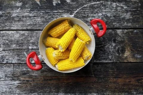Ears of corn boiled. corn in a saucepan on a wooden background. top view, flat Stock Photos