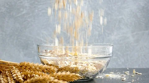 Ears of wheat and muesli falling into empty transparent glass bowl,slow motion Stock Footage 97710324