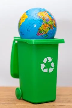 Earth globe sitting inside green recycling bin on wooden table Stock Photos