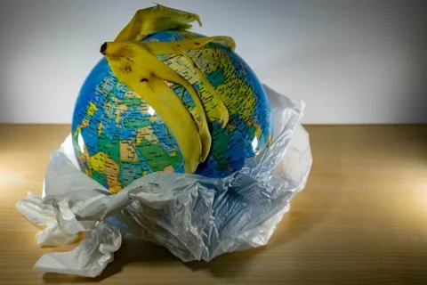 Earth inside a plastic and some garbage like paper and banana leftovers on to Stock Photos