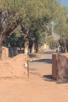 Earthen adobe gate opens to a quiet, tree-lined street Stock Photos
