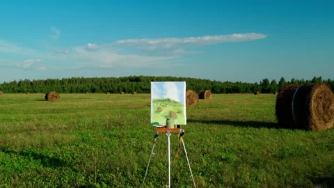 An easel with a painted landscape in an open field and bales of mown hay. Stock Footage 315738141