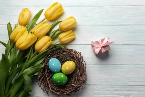 Easter background with bright, colored eggs in nest and yellow tulips. Top vi Stock Photos