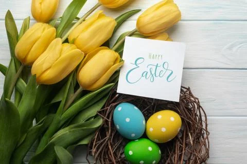 Easter background with bright, colored eggs in nest and yellow tulips. Top vi Stock Photos