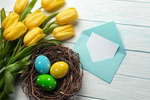 Easter background with bright, colored eggs in nest and yellow tulips. Top vi Stock Photos