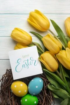 Easter background with bright, colored eggs in nest and yellow tulips. Top vi Stock Photos