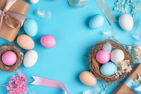 Easter background with colored eggs, nests, ribbons and feathers on a blue ba Stock Photos