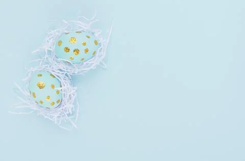 Easter background - easter eggs with golden dots in white nest on blue backdr Stock Photos
