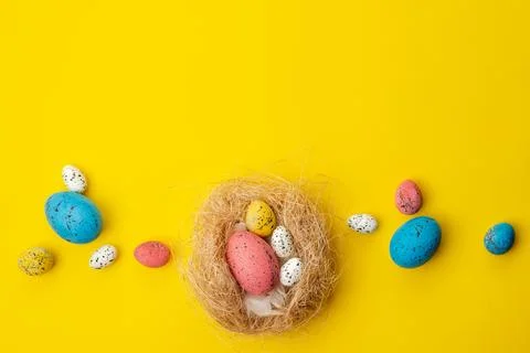 Easter background, multi-colored eggs in a nest lie on a yellow table. - Co.. Stock Photos