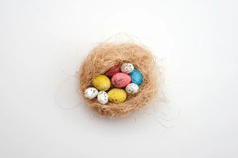 Easter background, multi-colored eggs in a nest lie on a white table Stock Photos
