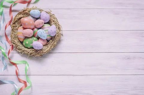 Easter background, a nest with painted eggs and colorful ribbons on a light wood Stock Photos