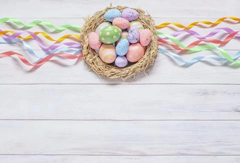 Easter background, a nest with painted eggs and colorful ribbons on a light wood Stock Photos