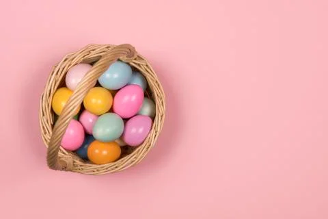 Easter background with pastel colored easter eggs in a basket on a pink backg Stock Photos