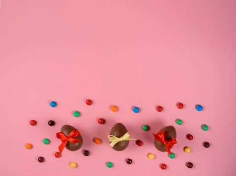 Easter background: three chocolate eggs among colorful dragee on the pink bac Stock Photos