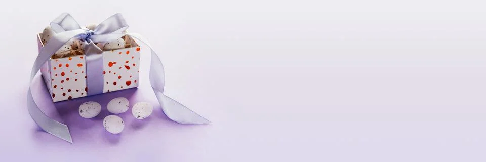 Easter banner with Easter eggs in a gift box with lavender blush ribbons on pale Stock Photos