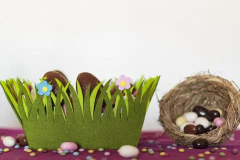 Easter basket with chocolate eggs and bird nest with easter almonds on table Stock Photos