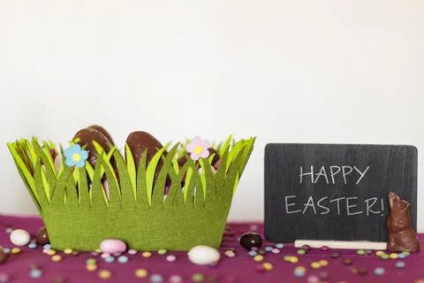 Easter basket with chocolate eggs, chocolate bunny missing a bite and blackbo Stock Photos