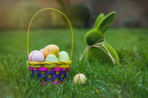 Easter basket with colored eggs and Easter bunny rabbit statuette on the green Stock-Fotos