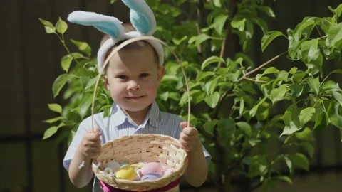 Easter boy portrait: cute kid boy Easter bunny ears holding basket Easter eggs Stock Footage 232541072
