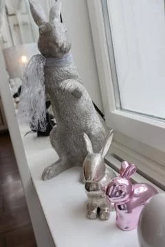 Easter bunnies sitting on sideboard in front of white bright window. Metal co Foto stock
