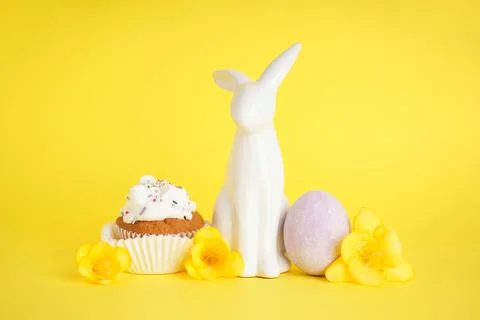 Easter bunny and delicious easter cupcake on yellow background. Stock Photos