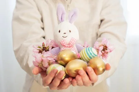 Easter bunny, colored eggs, and almond blossoms in hands. Easter preparations Stock Photos