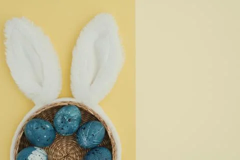 Easter bunny ears with blue easter eggs in wicker basket on two color yellow Stock Photos