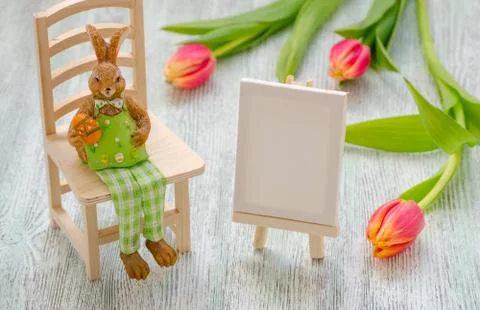 Easter bunny sitting on the stool with a egg, painting easel and tulips over Stock Photos