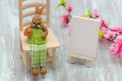 Easter bunny sitting on the stool with a egg, painting easel and flowers over Foto stock