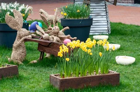 Easter bunny straw decorations in a spring garden with daffodils and eggs Stock Photos